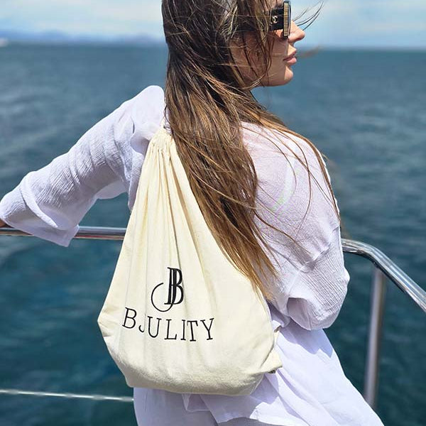 Frau Mit einem beigem Stoffbeutelrücksack mit goldenem BJULITY Logo auf einem Boot