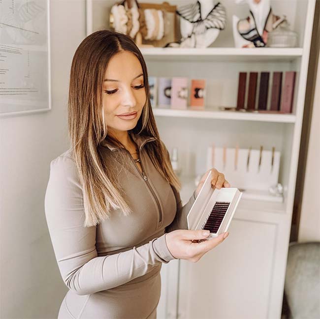 Frau präsentiert eine Packung Kunstwimpern. Im Hintergrund ist ein Regal mit Wimpernprodukten
