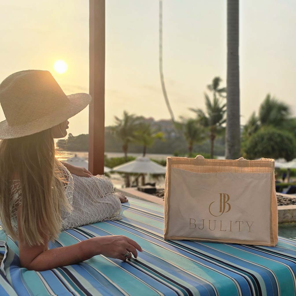 Frau mit Bjulity Totebag und Sommerhut auf einer Liege mit Sonnenuntergang im Hintergrund
